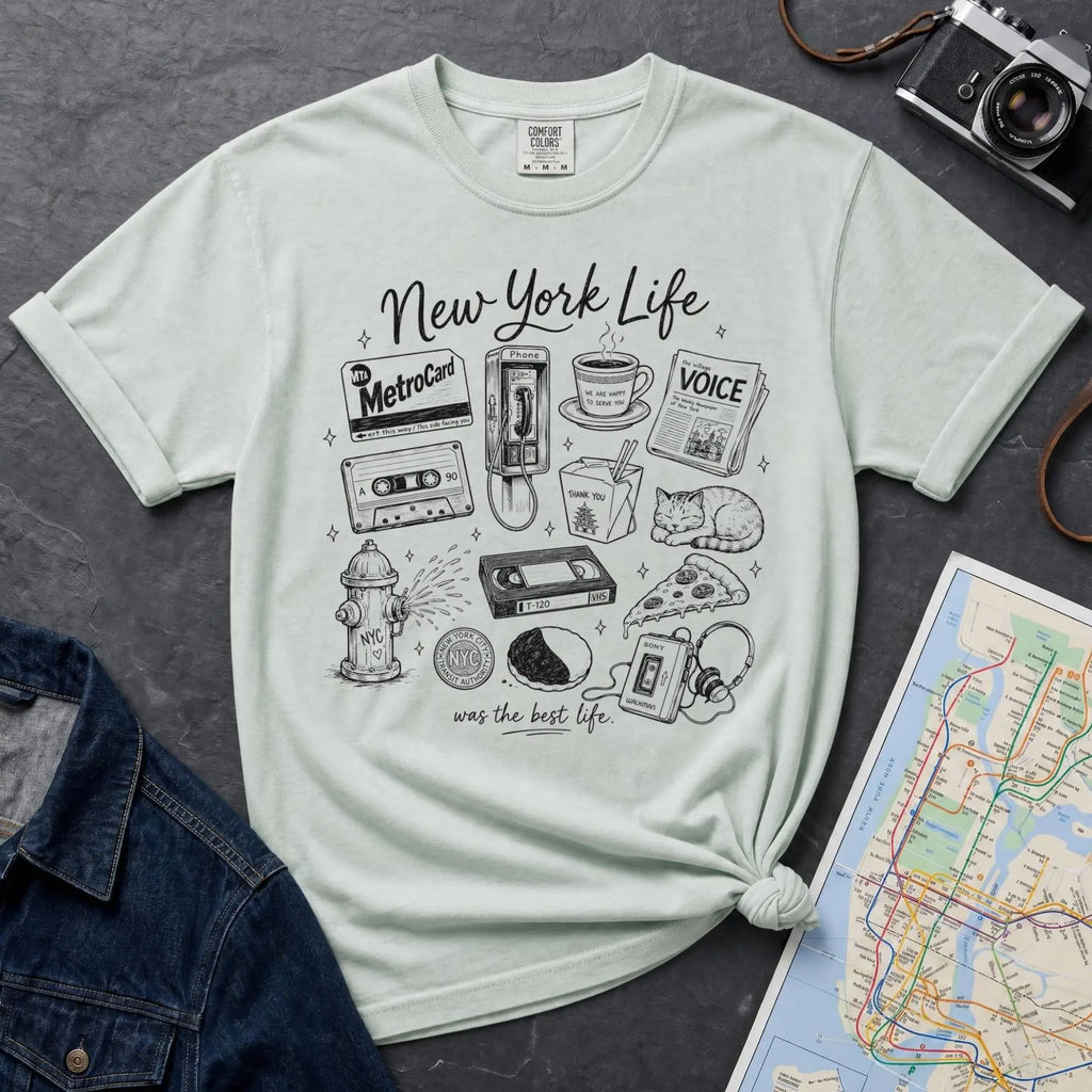 Bay colored t-shirt with New York-themed graphics on a gray surface with a map and camera.