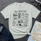 Bay colored t-shirt with New York-themed graphics on a gray surface with a map and camera.