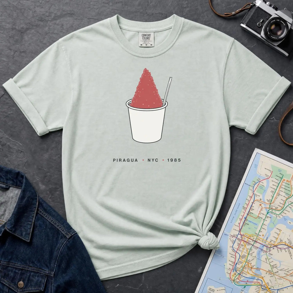 Bay colored Comfort Colors t-shirt with a piragua graphic and text, placed on a dark surface with a map and denim jacket.