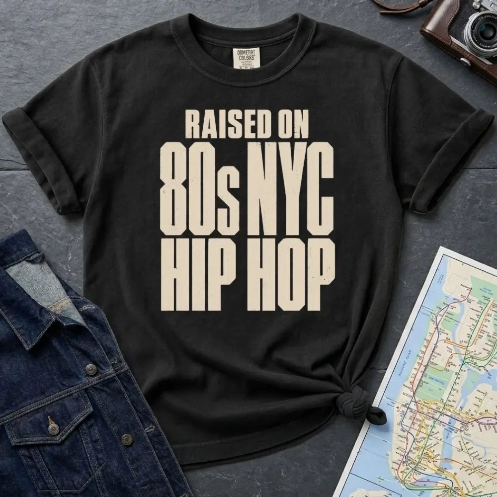 Black Comfort Colors T-shirt with cream Raised on 80s NYC Hip Hop front print, styled with denim jacket, camera, and subway map