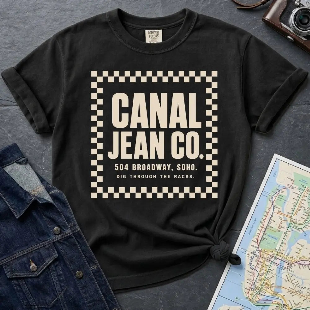 Black Comfort Colors T-shirt with ivory Canal Jean Co. NYC front print, styled with denim jacket, camera, and subway map.