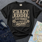 Black Comfort Colors t-shirt with distressed vintage retail graphic reading Crazy Eddie's Electronics in bold blocky lettering with lightning bolts and the tagline His Prices Are Insane, styled after 1980s NYC consumer electronics store signage.