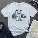 Light blue t-shirt with a Pitbull dog and cityscape design on a dark surface with jeans and a map.