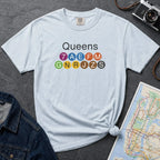 Light blue t-shirt with 'Queens' and NYC subway lines on a dark surface with a map and denim jacket.