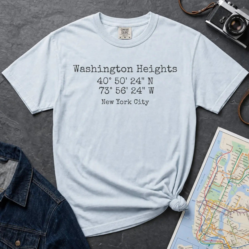 Light blue colored Comfort Colors t-shirt with 'Washington Heights' text with coordinates and 'New York City' on a dark surface with a map and denim jacket.
