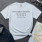 Light blue colored Comfort Colors t-shirt with 'Washington Heights' text with coordinates and 'New York City' on a dark surface with a map and denim jacket.