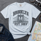 Light blue Vintage-style Brooklyn NYC graphic t-shirt on a Bay colored Comfort Colors cotton shirt, featuring the Brooklyn Bridge and “Brooklyn Est. 1883” text.