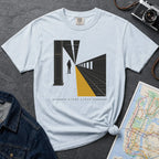 Light blue t-shirt with a graphic design of a train station platform, denim jacket, and map on a dark surface