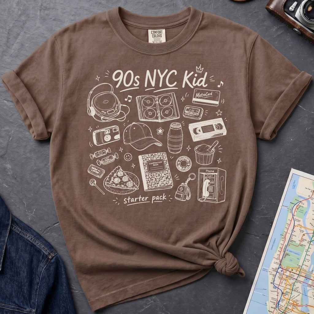 Espresso-colored Comfort Colors t-shirt with '90s NYC Kid' graphic design on a gray surface with a map and a denim jacket.