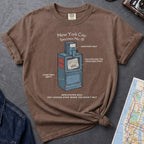 Brown t-shirt with a newspaper box graphic and text on a textured surface with a camera and map.