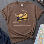 Brown t-shirt with New York City MetroCard graphic on a gray surface with a map and jacket.