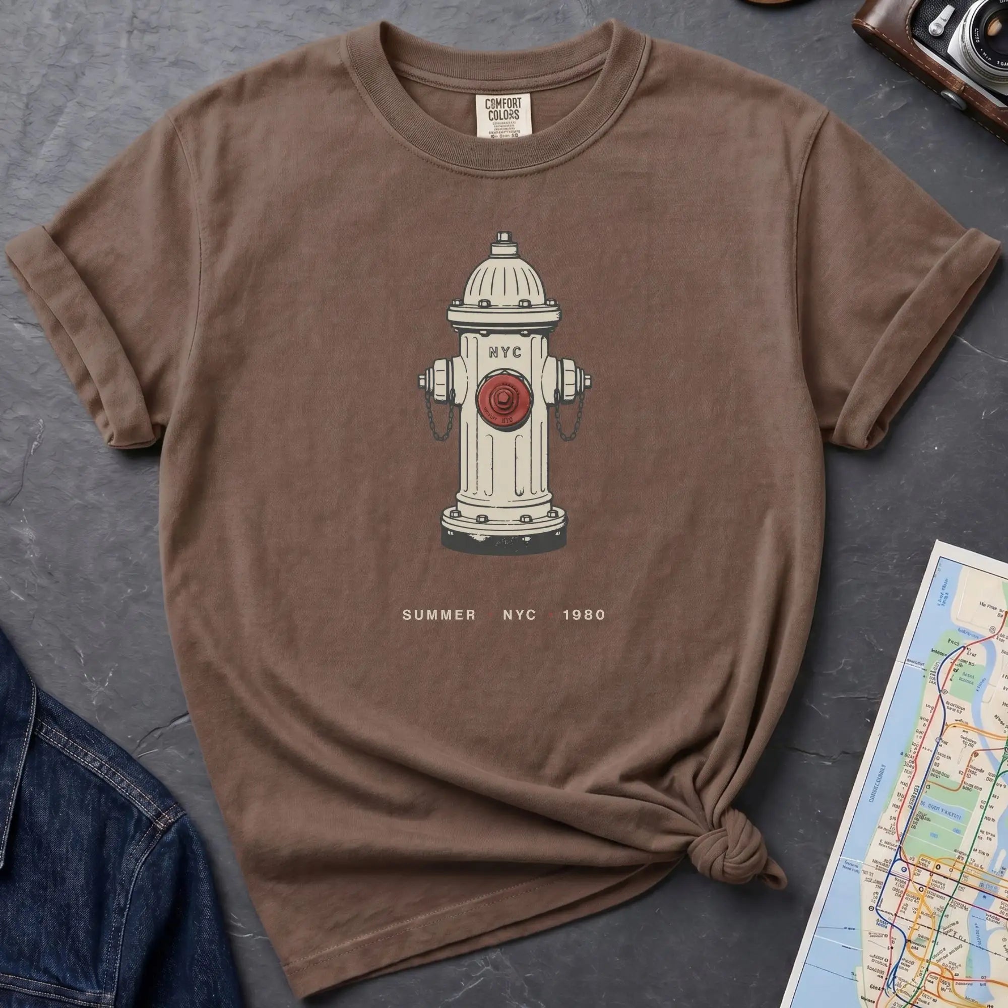 Brown t-shirt with a fire hydrant graphic on a gray surface with a map and jacket.