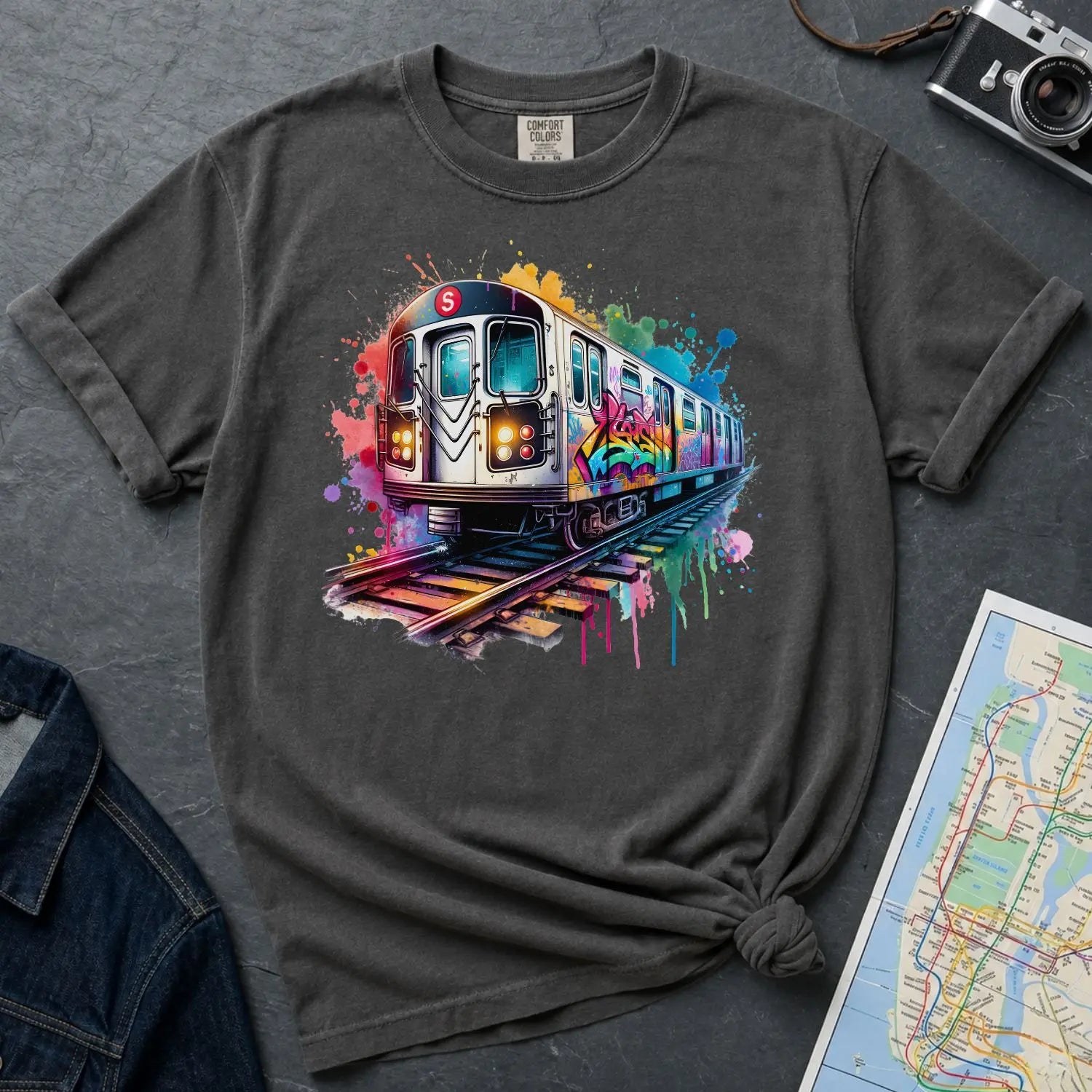Pepper colored Comfort Colors t-shirt with a colorful graffiti NYC subway train graphic on a gray surface with a camera and map.