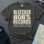 Pepper Colored Comfort Colors t-shirt with Bleecker Bob's Records in large distressed block lettering, London, New York, Hollywood and Open When Everyone Else Is Closed below, displayed on a flat surface with a denim jacket and subway map in the background.