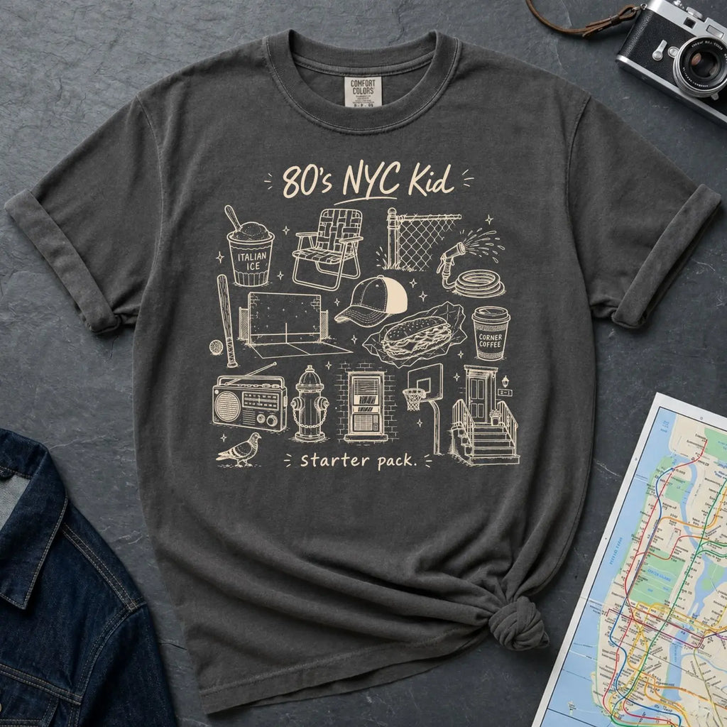 Pepper colored Comfort Colors t-shirt with '80's NYC Kid' graphic design on a dark surface with denim jacket and map.