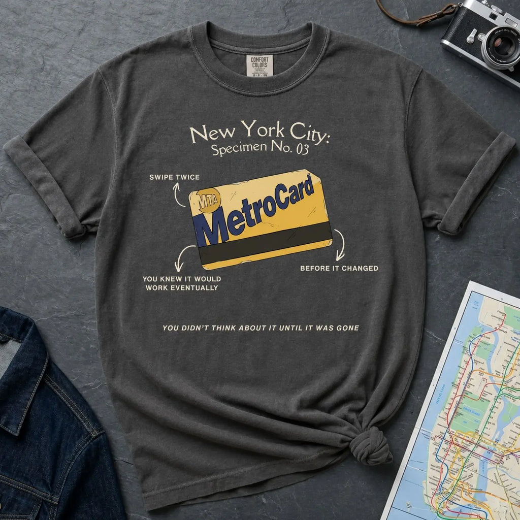 Pepper colored Comfort Colors t-shirt with New York City MetroCard graphic on a gray surface with a map and jacket.