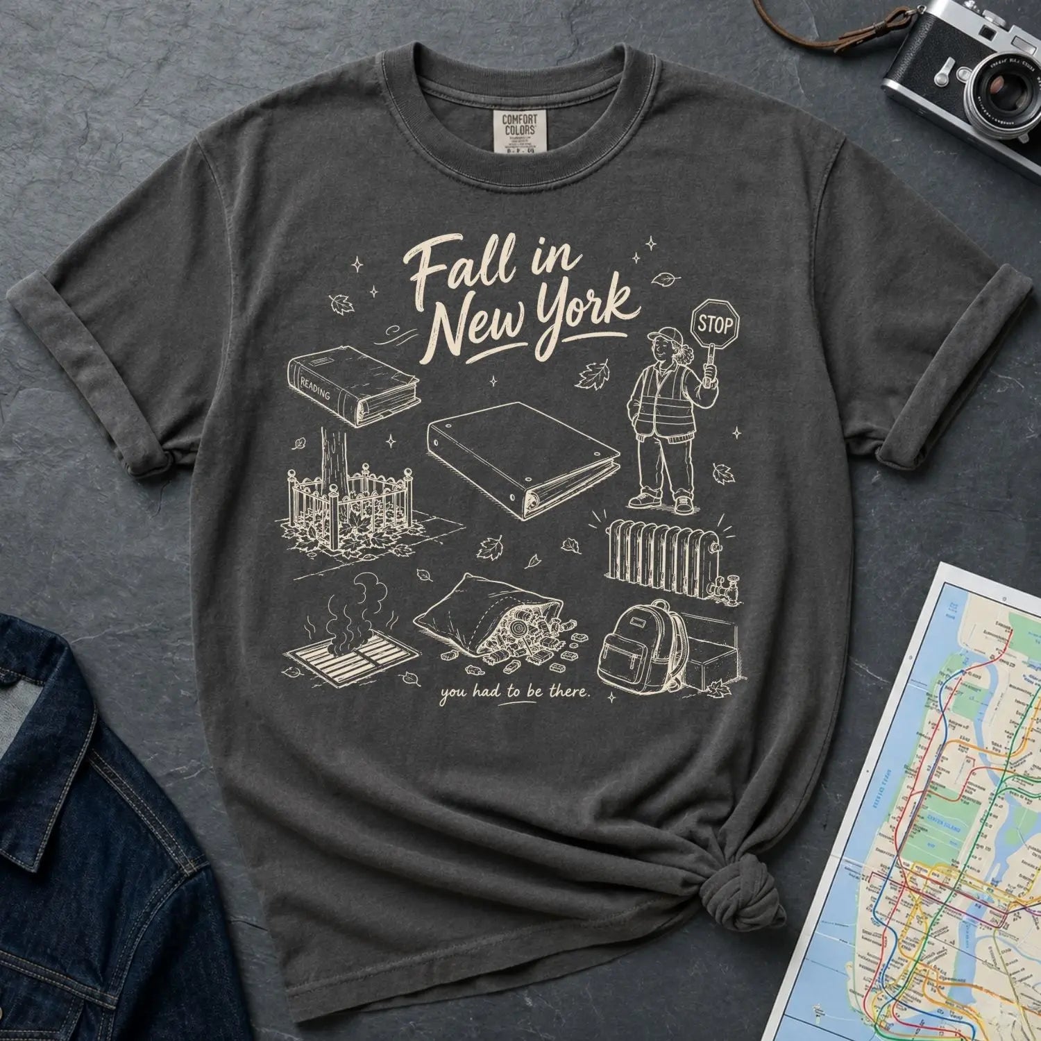 Pepper colored Comfort Colors t-shirt with 'Fall in New York' graphic design on a dark surface with a map and denim jacket.