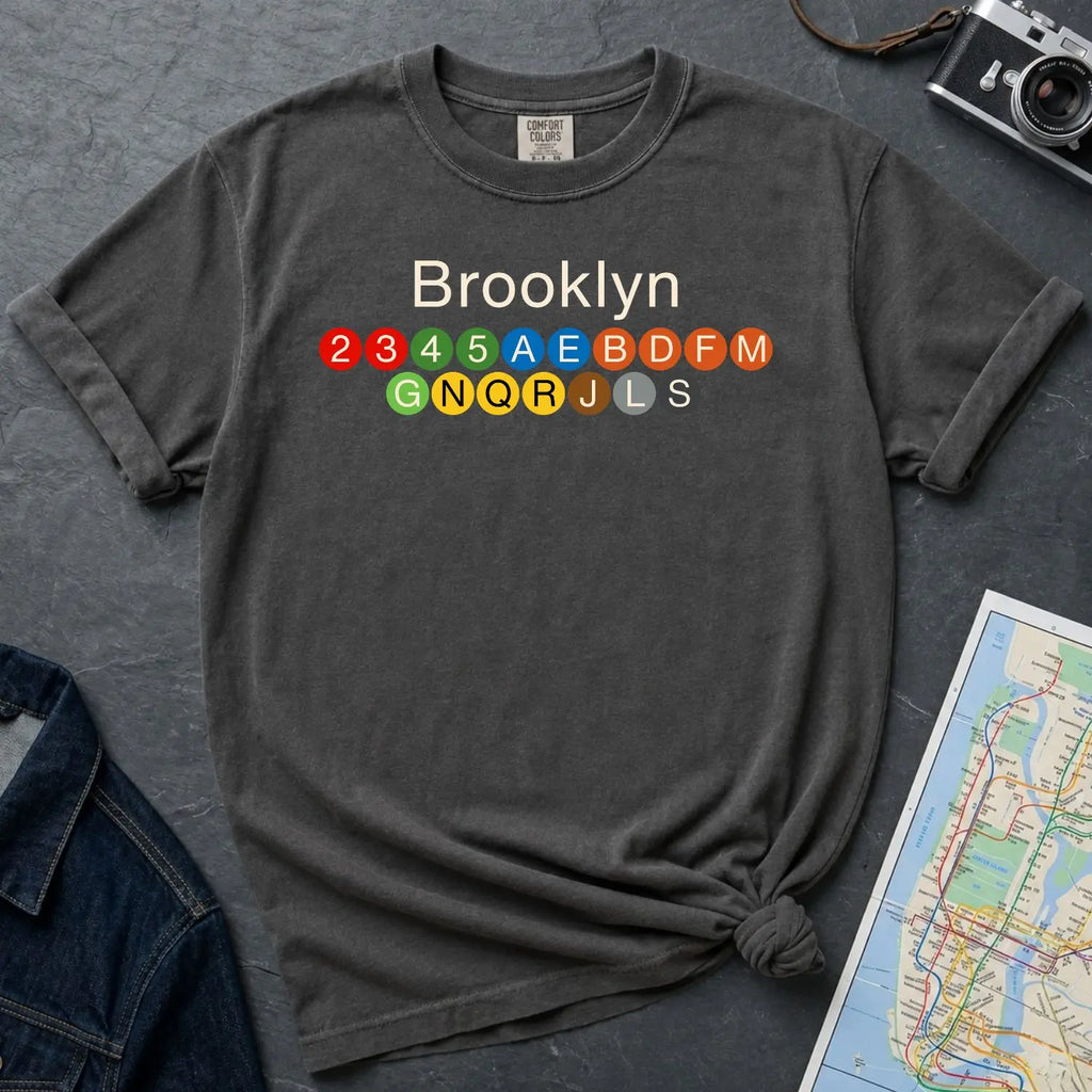 Pepper colored Comfort Colors t-shirt with 'Brooklyn' and subway lines on a dark surface with a map and camera.