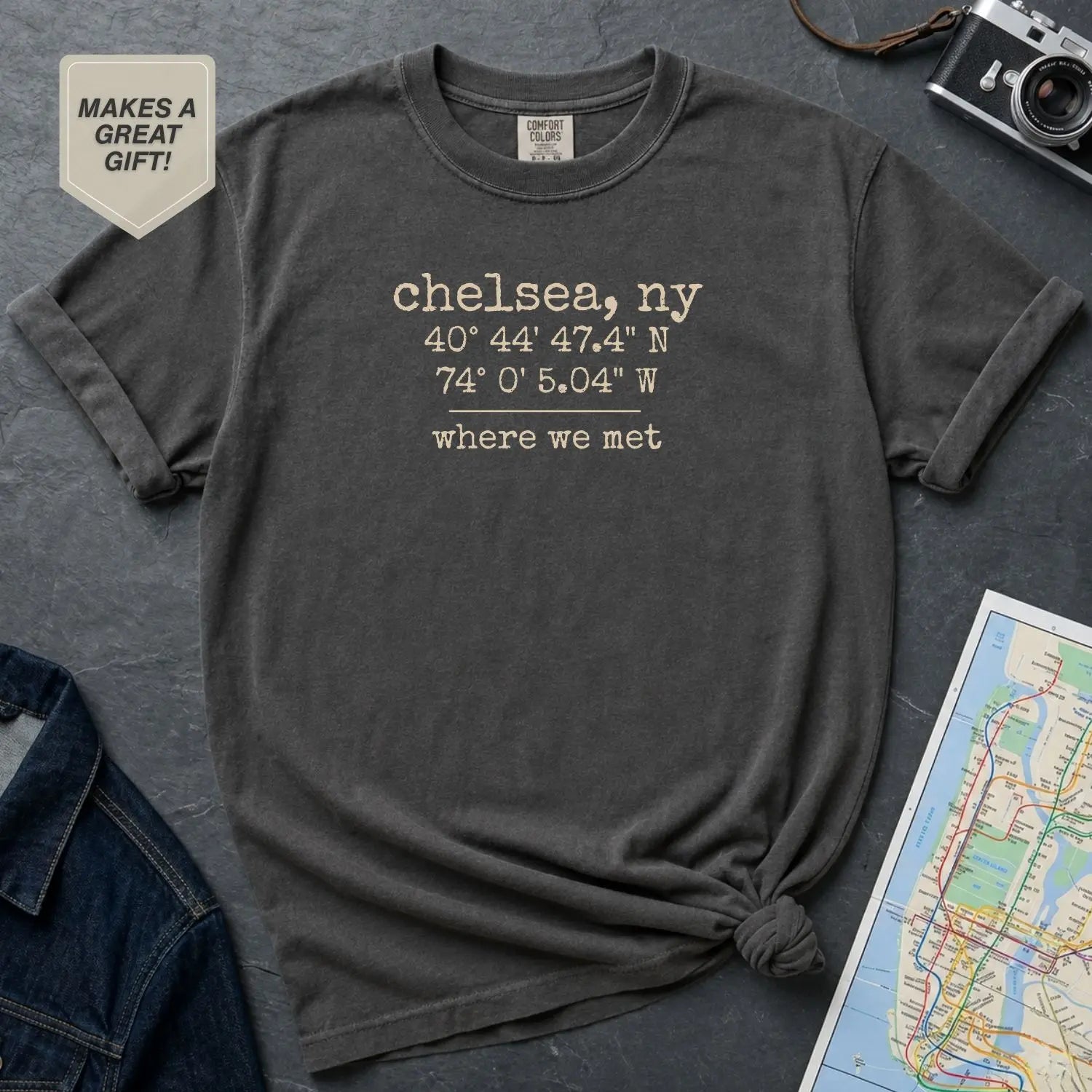 Pepper colored Comfort Colors t-shirt with coordinates and text 'chelsea, ny' and 'where we met' on a dark surface with denim jacket and map.