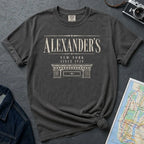Pepper colored Comfort Colors t-shirt with vintage serif lettering reading Alexander's, New York since 1928, above an illustrated stone building cornice, styled after a classic 1920s Bronx department store facade.