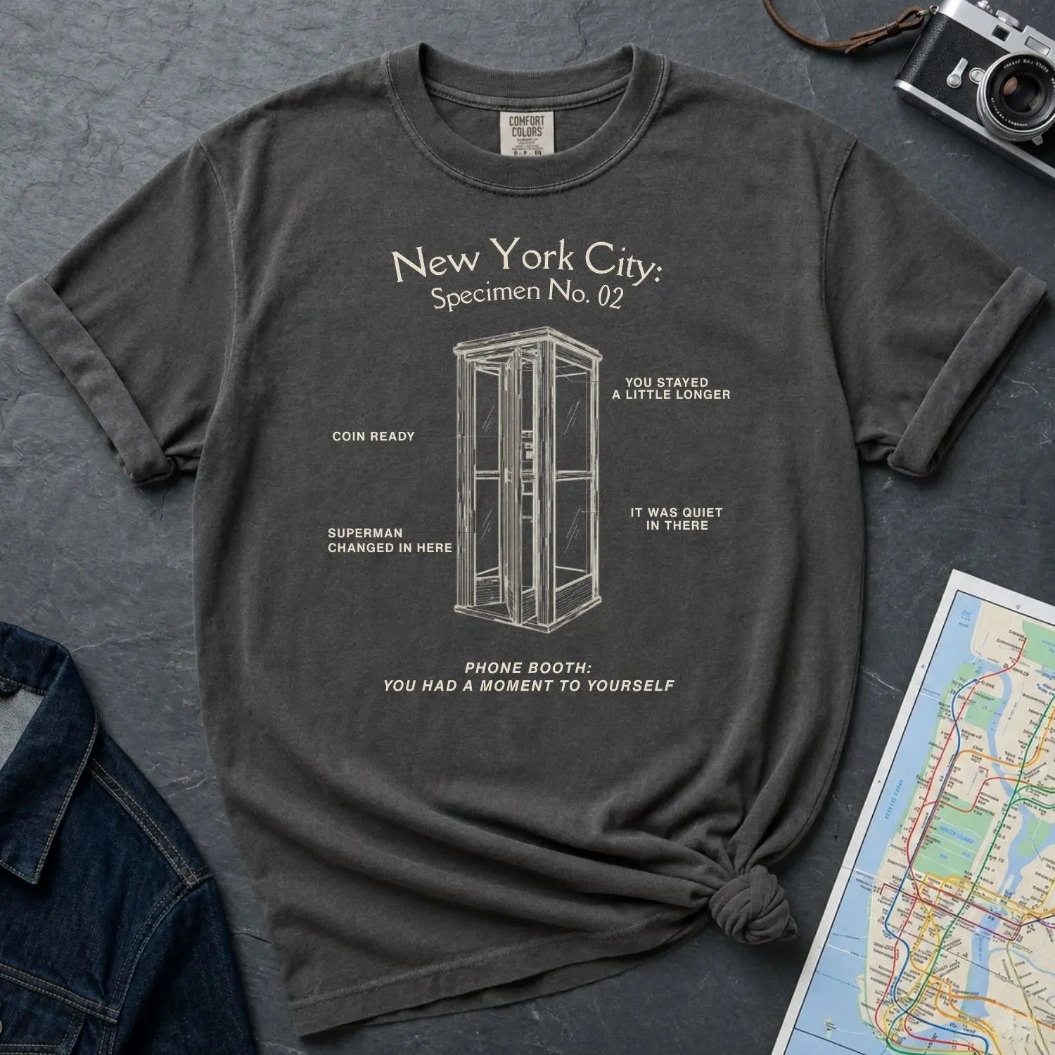 Pepper colored Comfort Colors t-shirt with phone booth design and text on a dark surface with denim jacket and map.