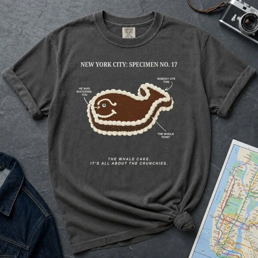 Pepper-colored Comfort Colors T-shirt with NYC whale cake specimen front print, styled with denim jacket, camera, and subway map