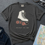 Pepper colored Comfort Colors t-shirt featuring a vintage roller skate graphic with “Roll With It • NYC • 1988” text placed on a textured surface with a camera and map.