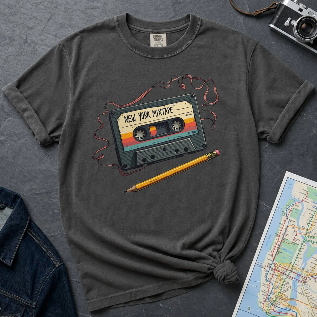 Pepper colored t-shirt with a cassette tape graphic and pencil on a gray surface with denim jacket and map.