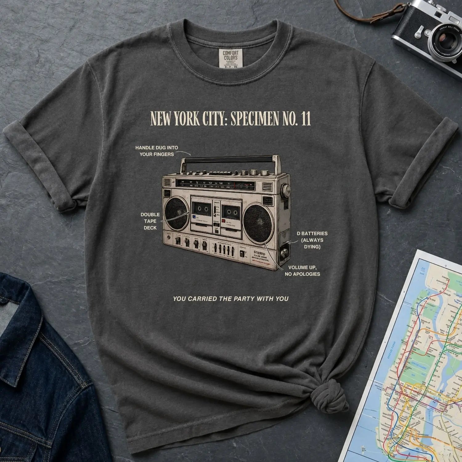 Pepper colored Comfort Colors t-shirt with a graphic of a boombox and text on a dark surface with a denim jacket and map.