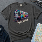 Pepper colored Comfort Colors t-shirt with a graffiti train graphic and 'New York' text on a textured surface with a map and camera.