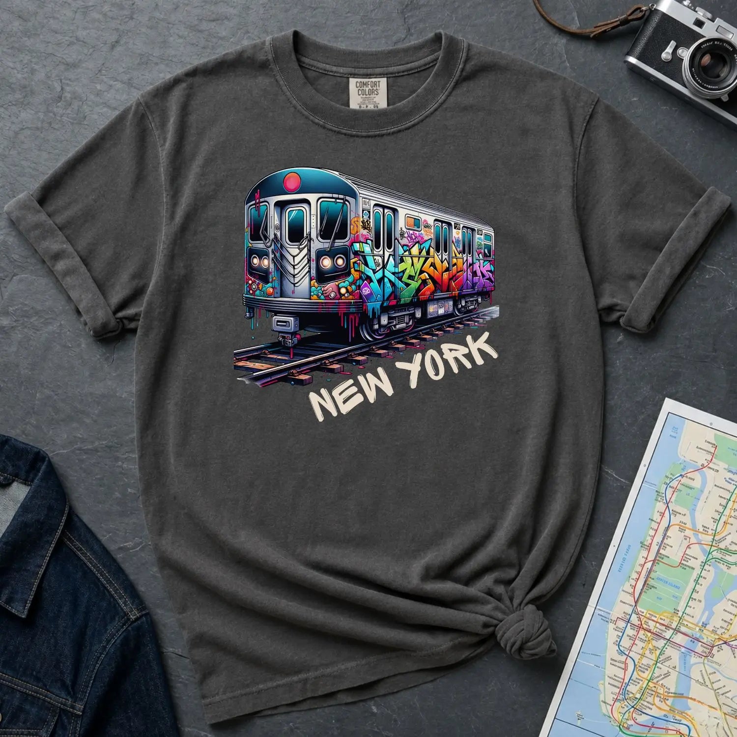 Pepper colored Comfort Colors t-shirt with a graffiti train graphic and 'New York' text on a textured surface with a map and camera.