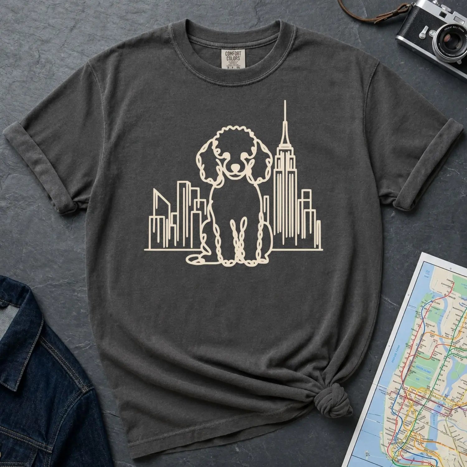 Pepper colored Comfort Colors t-shirt with a Poodle and cityscape design on a dark surface with a denim jacket and a map.