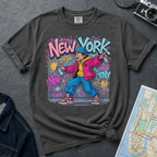 Pepper colored Comfort Colors t-shirt featuring a colorful NYC graffiti-style New York graphic with a young street artist holding a spray paint can design on a gray surface with denim jacket and map.