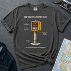 Pepper colored Comfort Colors t-shirt with a graphic design of a vintage intersection crossing sign and text, placed on a dark surface with a denim jacket and a map.