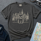 Pepper colored Comfort Colors t-shirt with a Maltese dog and cityscape design on a gray surface with a map and camera.