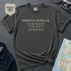 Pepper colored Comfort Colors t-shirt with text 'astoria park, ny', coordinates and 'our first kiss', placed on a dark surface with a map and denim jacket.
