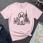 Pink t-shirt with a poodle and cityscape design on a dark surface with a map and camera.