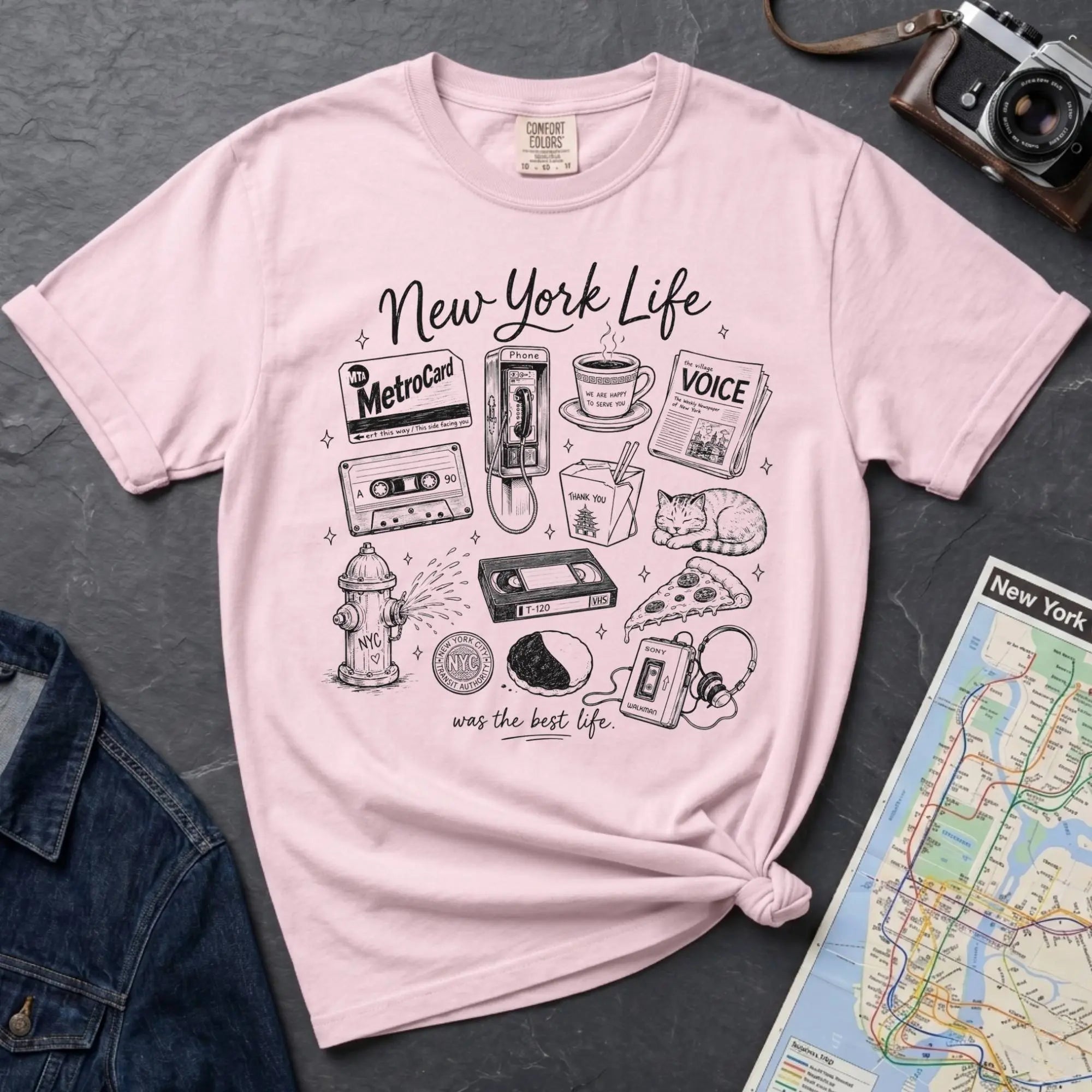Pink t-shirt with New York-themed graphics on a gray surface with a map and camera.