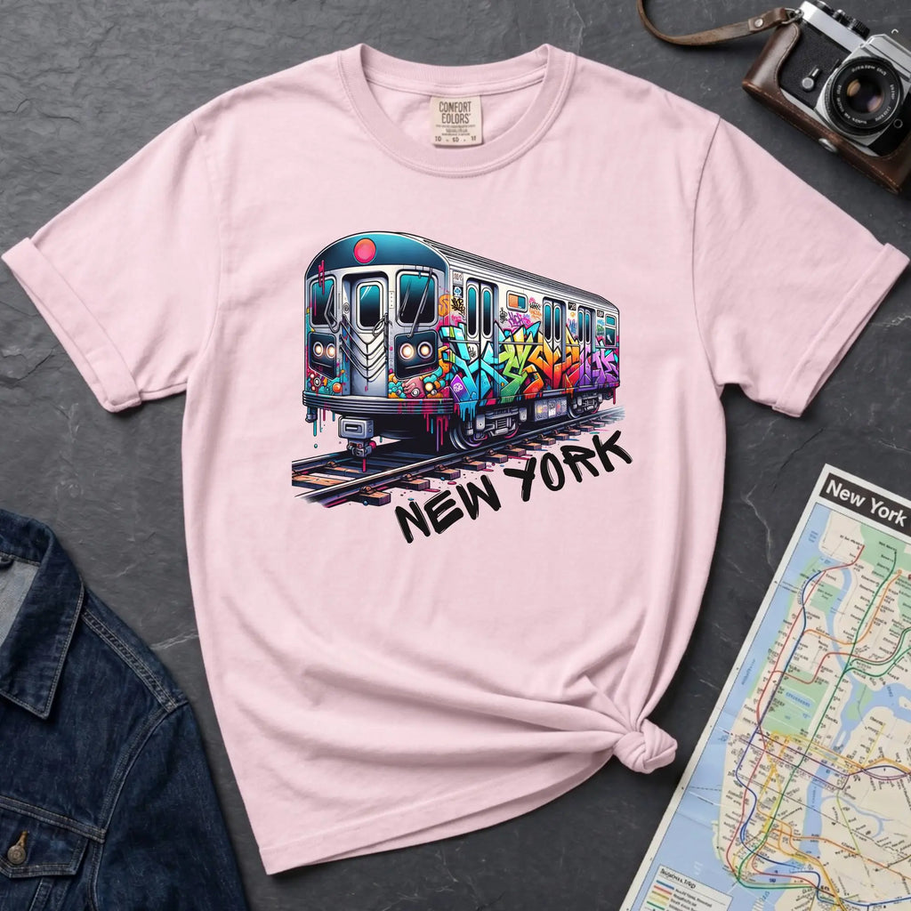 Pink t-shirt with a colorful train graphic and 'New York' text on a gray surface with a map and denim jacket.