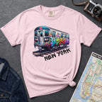 Pink t-shirt with a colorful train graphic and 'New York' text on a gray surface with a map and denim jacket.