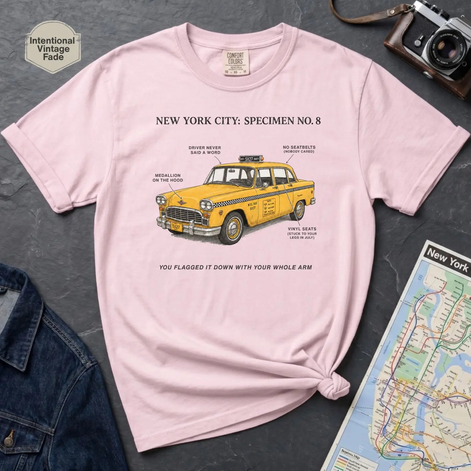 Pink Comfort Colors t-shirt with yellow taxi graphic and text on a dark surface with denim jacket and map.