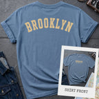 Light blue colored Comfort Colors t-shirt with 'Brooklyn' printed on the back and 'Brooklyn, New York City', on a dark surface. 