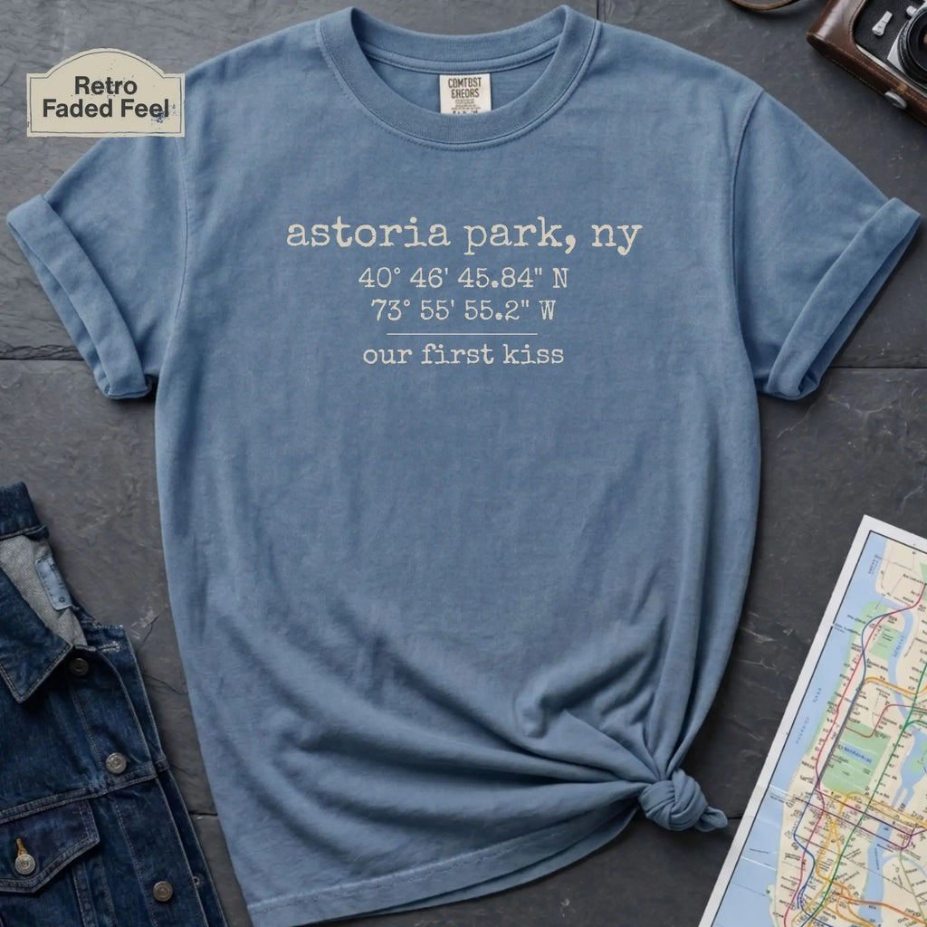 Blue t-shirt with text 'astoria park, ny' and coordinates on a dark surface with denim jacket and map.