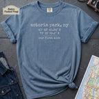 Blue t-shirt with text 'astoria park, ny' and coordinates on a dark surface with denim jacket and map.