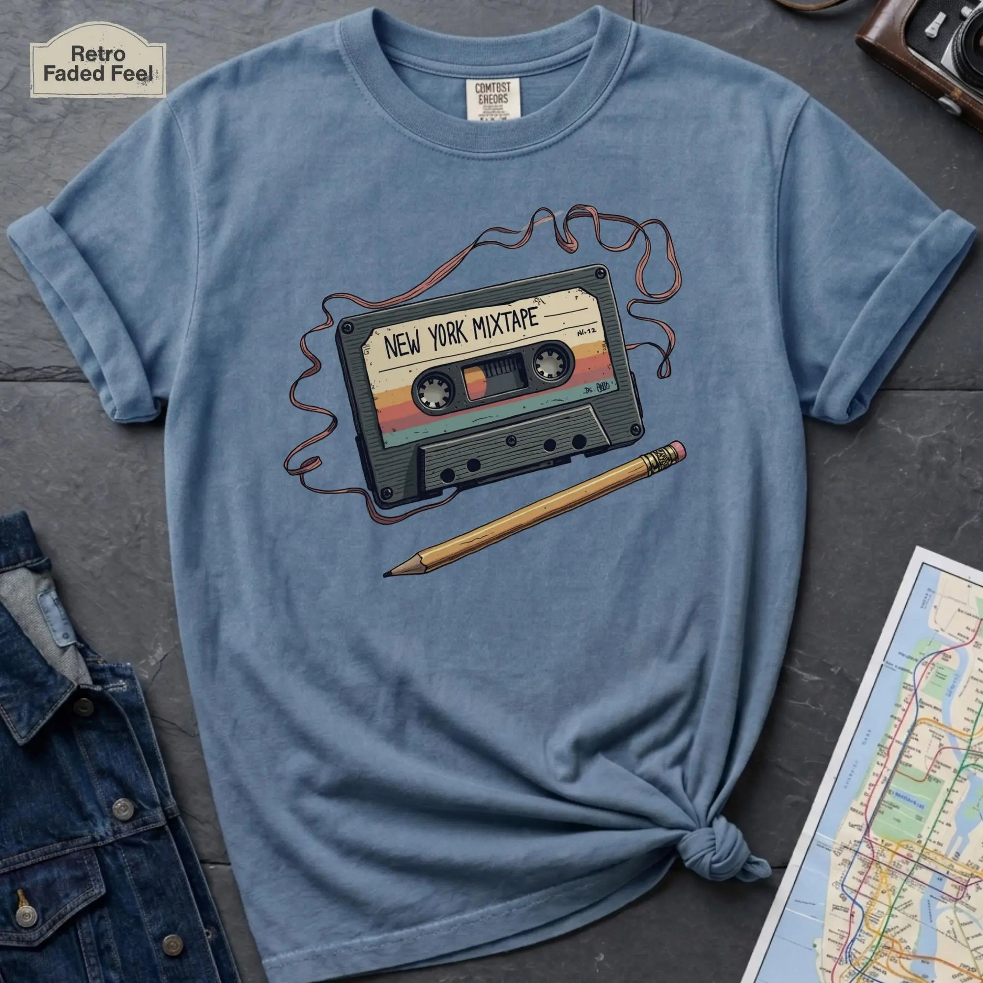 Blue t-shirt with a cassette tape and pencil graphic on a dark surface.