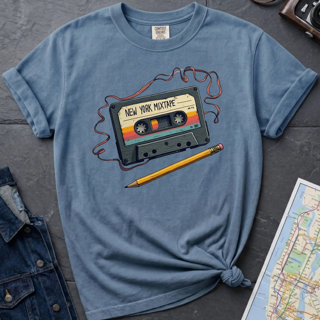 Blue t-shirt with a cassette tape graphic and pencil on a gray surface with denim jacket and map.
