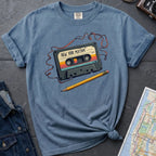 Blue t-shirt with a cassette tape graphic and pencil on a gray surface with denim jacket and map.