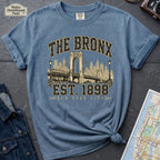 Blue t-shirt with 'The Bronx Est. 1898' design on a dark surface with a map and a denim jacket.