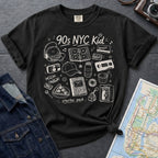 Black Comfort Colors t-shirt with '90s NYC Kid' graphic design on a dark surface with denim jacket and map.
