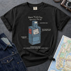 Black t-shirt with a newspaper box graphic and text on a textured surface with a camera and map.